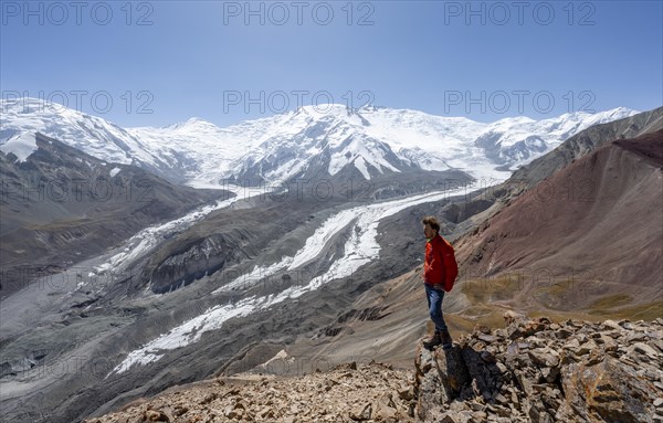 Mountaineer at Traveller's Pass with view of impressive mountain landscape, high mountain landscape with glacier moraines and glacier tongues, glaciated and snow-covered mountain peaks, Lenin Peak and Peak of the XIX Party Congress of the CPSU, Trans Alay Mountains, Pamir Mountains, Osh Province, Kyrgyzstan, Asia