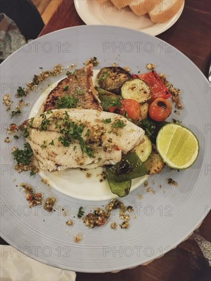 Grilled trout fish on a bed of quinoa with roasted vegetables and a lime wedge, healthy low-carb meal