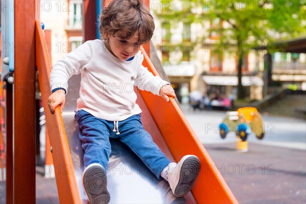 A small girl sliding down a slide in an urban playground
