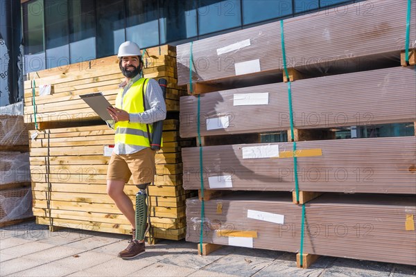 Engineer with prosthetic leg working outdoors with paperwork in a construction site leaning on a wall