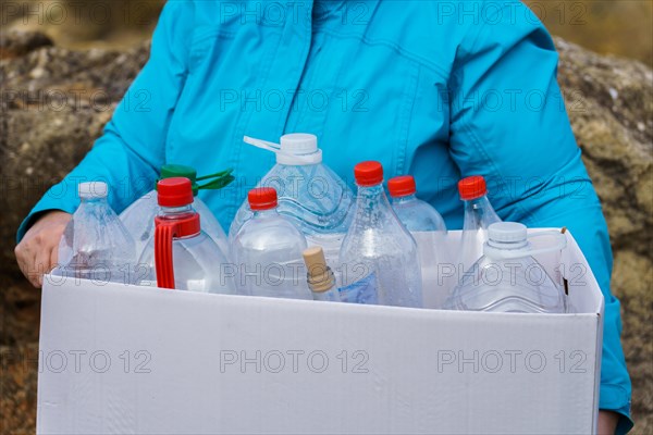 Woman holding a white cardboard box full of empty plastic bottles for recycling, environmental protection and ecology concept