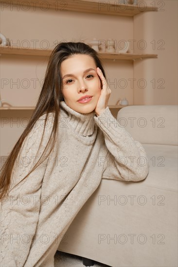 Lovely beautiful woman in warm sweater sitting next to a couch with her hand on her head