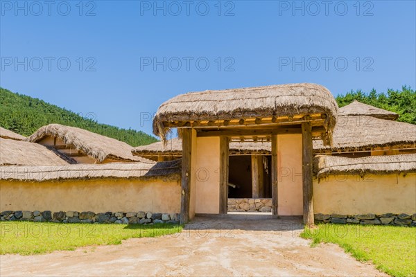 Buyeo, South Korea, July 7, 2018: Front gate of Korean village with building built of wood and straw thached roofs behine stone wall in public park at at Neungsa Baekje Temple. For editorial use only, Asia
