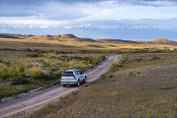 An SUV drives along a gravel track through an open steppe landscape, Kyrgyzstan, Asia
