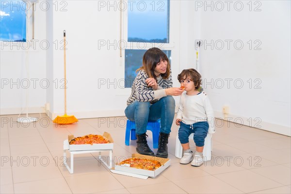 Mother and child eating pizza in an empty house after moving