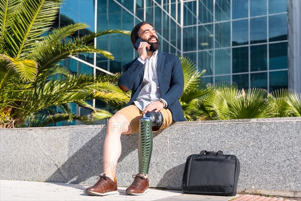 Businessman with prosthetic leg smiling talking to the mobile sitting outside a financial building