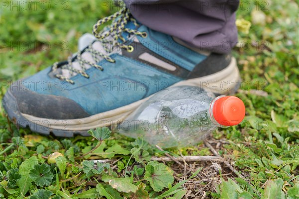 Hiking boot stepping on an empty plastic bottle on the green grass of a meadow, ecology and environment concept