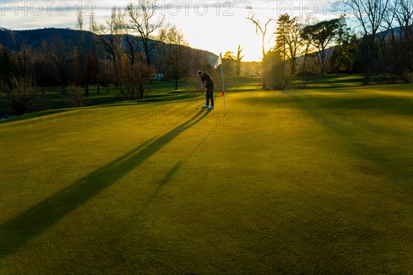 Male Golfer Concentration on the Putting Green on Golf Course in Sunset with Shadow in Switzerland