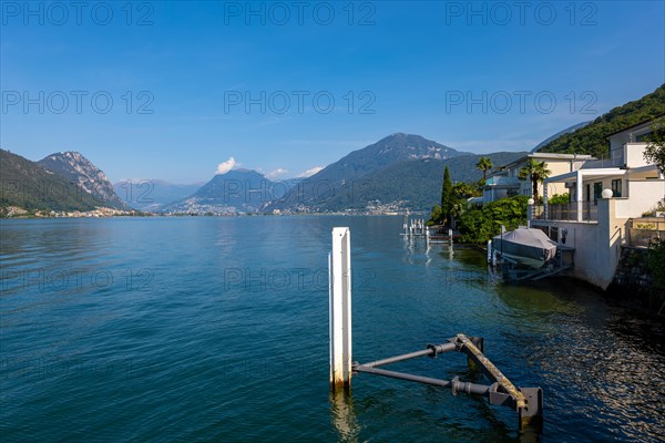 Pier and Houses in Brusino Arsizio on the Waterfront in a Sunny Summer Day on Lake Lugano with Mountain in Brusino Arsizio, Ticino, Switzerland, Europe