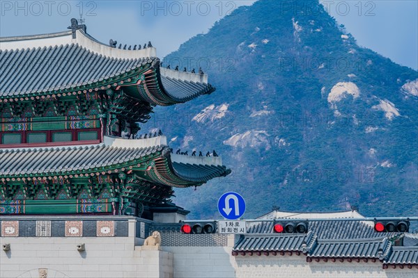 Seoul, South Korea, March 18, 2017:Tiled roof of Seoul's Gyeong Bok Gung Palace in stunning colors with a traffic light and sign that says one lane left u-turn in Korean language and a mountain in the background, Asia