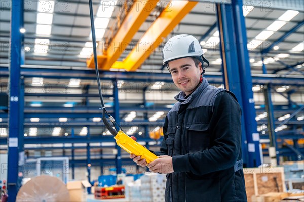 Engineer with protective hard hat controlling an industrial crane with control remote