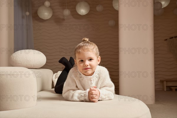 Cute little caucasian child lying on her stomach on sofa