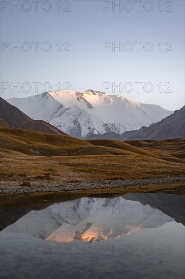 White glaciated and snowy mountain peak Pik Lenin at sunset, mountains reflected in a lake between golden hills, Trans Alay Mountains, Pamir Mountains, Osh Province, Kyrgyzstan, Asia