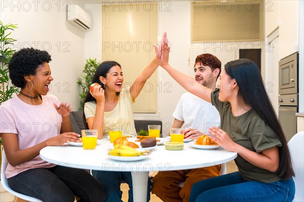 Multi-ethnic friends celebrating while high-fiving during breakfast together at home