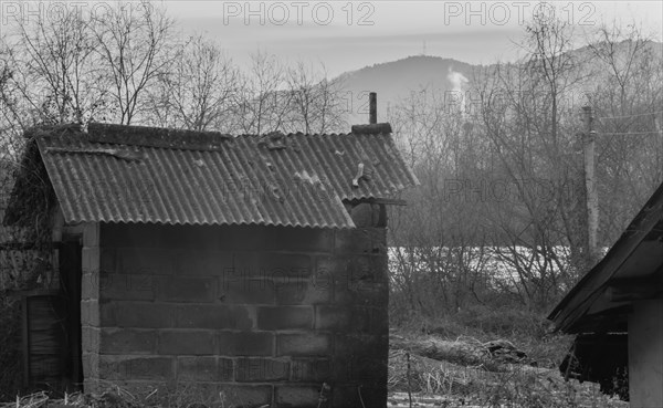 Black and white of small sod storage building in rural setting with sun bouncing off the atmosphere and smoke from chimney in background