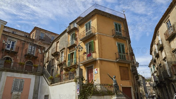 A street corner in a town with a bronze statue and traditional balconies, Novara di Sicilia, Sicily, Italy, Europe