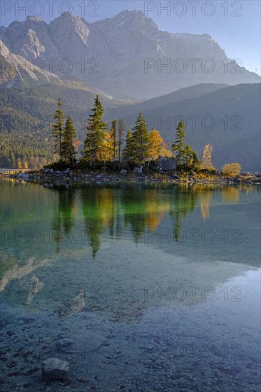 Reflection of an island in a mountain lake in front of steep mountains, autumn, evening light, Eibsee lake, Zugspitze, Bavaria, Germany, Europe