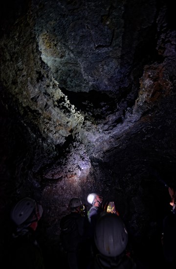 Cave explorers in the lava tunnel Gruta das Torres with helmets looking at an illuminated rock face in the dark, Gruta das Torres, Pico Island, Azores, Portugal, Europe