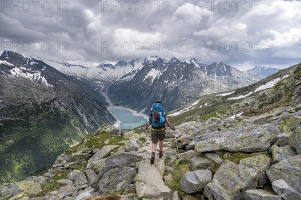 Mountaineer on hiking trail, view of Schlegeisspeicher, glaciated rocky mountain peaks Hoher Weisszint and Hochfeiler with glacier Schlegeiskees, Berliner Hoehenweg, Zillertal Alps, Tyrol, Austria, Europe