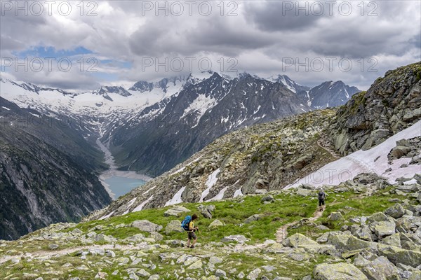 Two mountaineers on hiking trail, view of Schlegeisspeicher, glaciated rocky mountain peaks Hoher Weisszint and Hochfeiler with glacier Schlegeiskees, Berliner Hoehenweg, Zillertal Alps, Tyrol, Austria, Europe