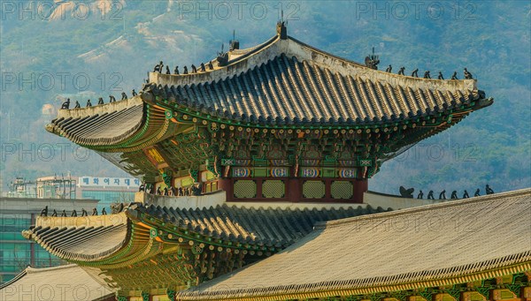 Seoul, South Korea, March 18, 2017:Tiled roof of Gyeong Bok Gung Palace in stunning colors with small figurines on the eves set against a background of a mountain side with visible boulders, Asia