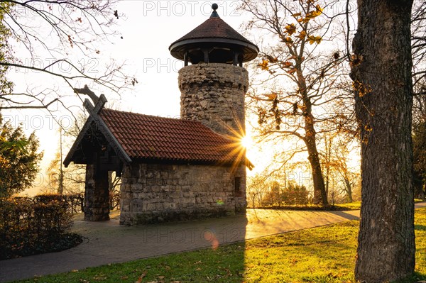 Historic tower backlit by the sunrise, surrounded by autumnal trees, Hachelturm, Pforzheim, Germany, Europe
