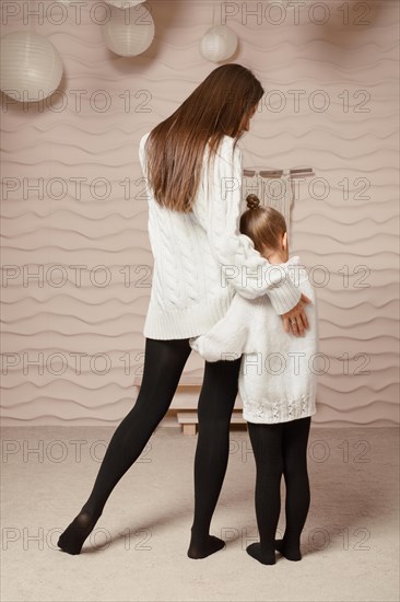 A rear view of a little girl clinging to her mother and hugging her hip