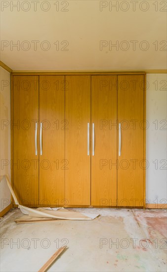Wooden doors with metal handles of built-in closets in bedroom with debris and trash on floor in abandoned house