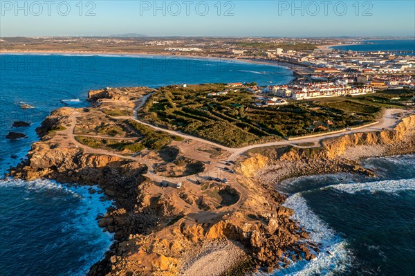 Peniche peninsula with high cliffs and ocean tide at sunset, Portugal. Summer sunset haze, little foliage and rocky cliffs, peninsula and rocks, fishing town, horizon