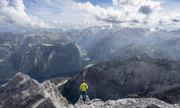 Mountaineer on the rocky summit of the Watzmann Mittelspitze, Watzmann crossing, view of mountain panorama with Steinernes Meer and Koenigssee, Berchtesgaden National Park, Berchtesgaden Alps, Bavaria, Germany, Europe