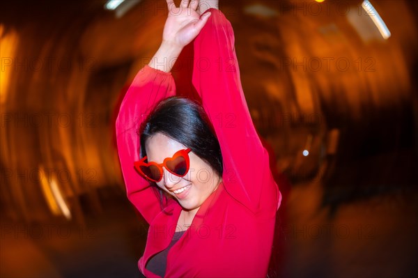 Night photo with flash and motion of fashionable woman with heart shape sunglasses dancing in the street at night