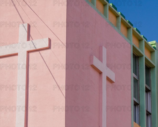 Crosses on side of a pink stucco building with power lines casting shadow on building