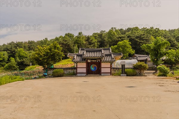 Daejeon, South Korea, May 22, 2018: Korean woman sitting under tree in front of stone wall attached to gate of Korean style building, Asia