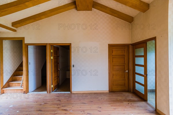 Living room with wood beam ceiling and doors leading to other rooms in two story abandoned house