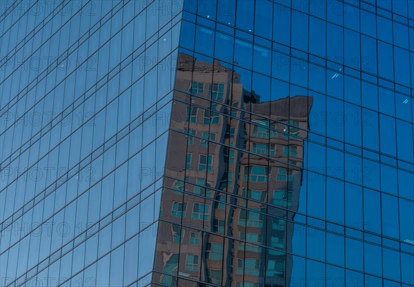 Low angle view of glass office building with reflection of brick building in side windows on sunny day