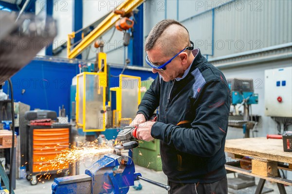 Worker wearing safety gear and eyeglasses using an electric disc to cut metal