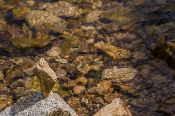 Large rock shaped like a thumb balanced on top of another larger stone at edge of shallow river