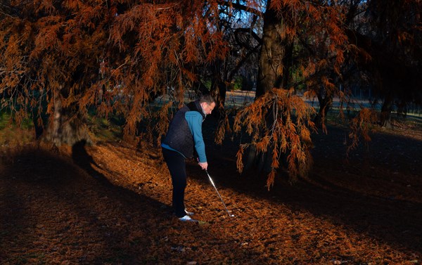 Male Golfer Below an Autumn Tree and Hitting His Golf Ball on Golf Course in a Sunny Day in Switzerland