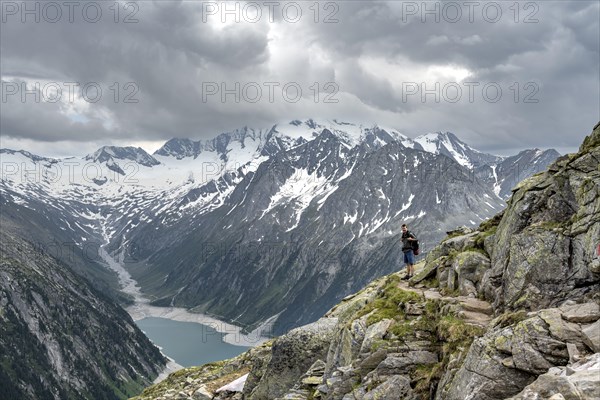 Mountaineer on hiking trail, view of Schlegeisspeicher, glaciated rocky mountain peaks Hoher Weisszint and Hochfeiler with glacier Schlegeiskees, Berliner Hoehenweg, Zillertal Alps, Tyrol, Austria, Europe