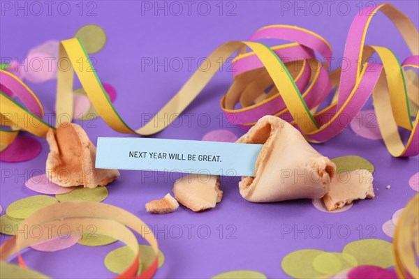 Optimistic Silvester New Year celebration concept with open fortune cookie and text 'Next year will be great' on colorful background with paper streamers and confetti
