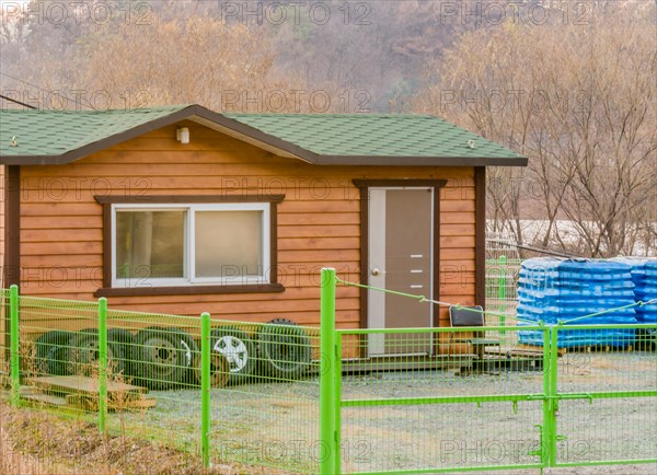 Small wooden storage shed with green asphalt roof surrounded by a green chain link fence