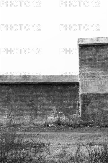 Black and white of small wire-frame and stucco building in countryside. Building has no window or doors