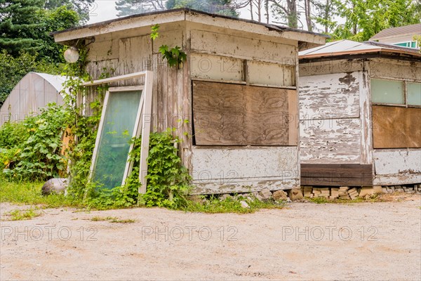 Abandoned and shuttered lake cabins with gravel parking lot in foreground