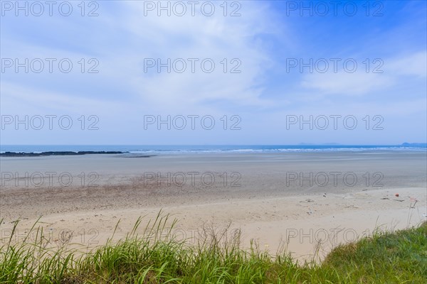 Landscape of sandy beach with rocky shore line under blue sky with cirrus clouds