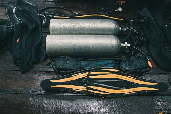 Scuba diving gear neatly arranged on a wooden floor, including fins and tanks