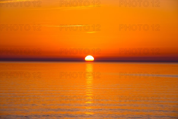 Intense, atmospheric sunset with bright orange-yellow sky over the Baltic Sea, reflection of the light in the calm water, Hiddensee Island, Mecklenburg-Western Pomerania, Germany, Europe