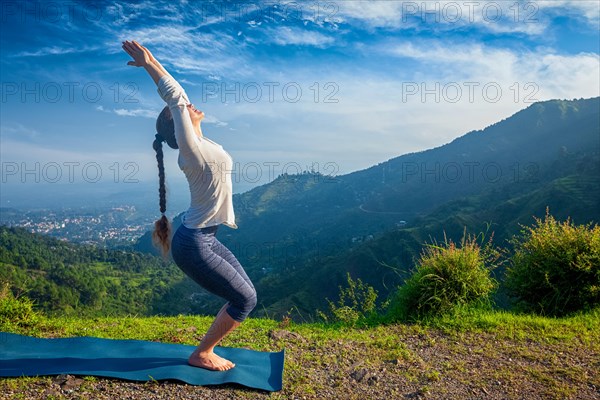 Young woman doing yoga asana Utkatasana (chair pose) outdoors in mountains Himalayas in the morning. Himachal Pradesh, India, Asia