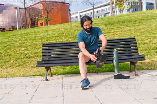 Physically disabled male runner adjusting prosthetic leg sitting on a bench in a park