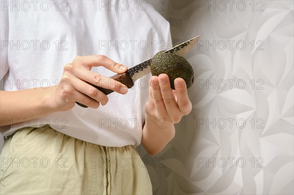 Low angle view at hands of woman cutting fresh avocado with knife in the kitchen