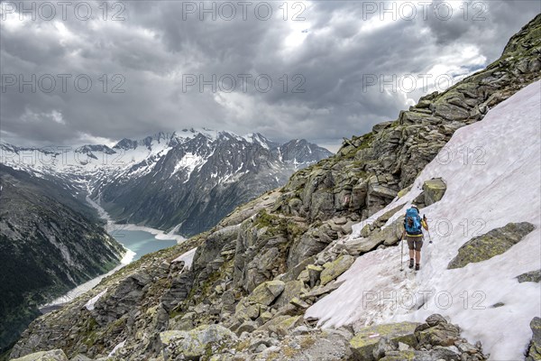 Mountaineer on hiking trail with snow, view of Schlegeisspeicher, glaciated rocky mountain peaks Hoher Weisszint and Hochfeiler with glacier Schlegeiskees, Berliner Hoehenweg, Zillertal Alps, Tyrol, Austria, Europe